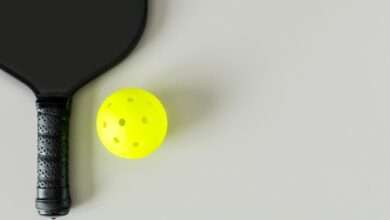 A black pickleball paddle and neon yellow ball on a light gray surface, viewed from above, with subtle shadows.
