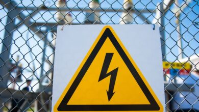 A yellow high-voltage warning sign with a black lightning bolt mounted to a chain-link fence at an electrical substation.