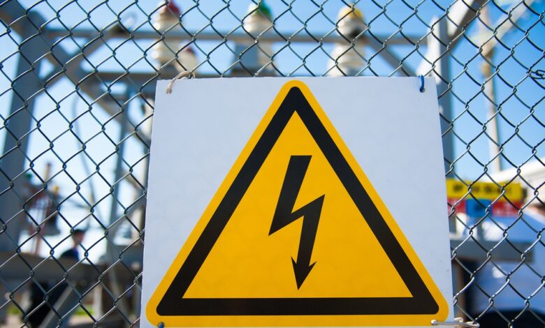 A yellow high-voltage warning sign with a black lightning bolt mounted to a chain-link fence at an electrical substation.
