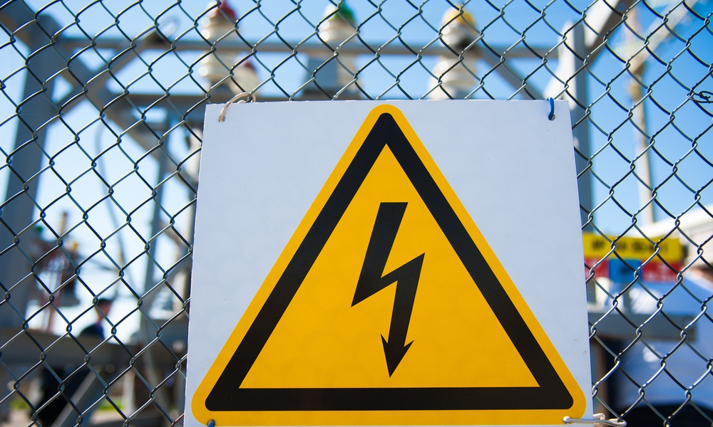 A yellow high-voltage warning sign with a black lightning bolt mounted to a chain-link fence at an electrical substation.