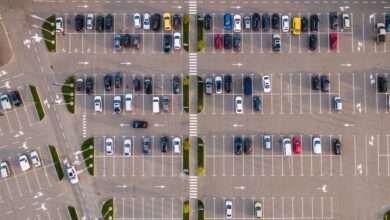 An aerial view of a commercial parking lot. There are many cars parked and they are all of varying colors and designs.