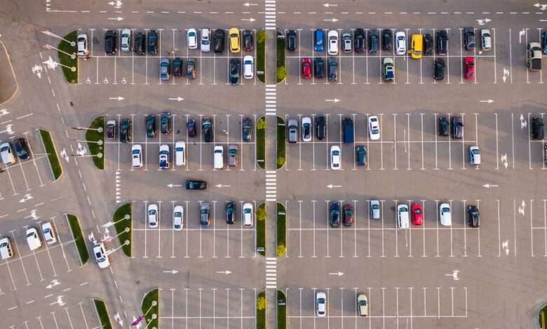An aerial view of a commercial parking lot. There are many cars parked and they are all of varying colors and designs.