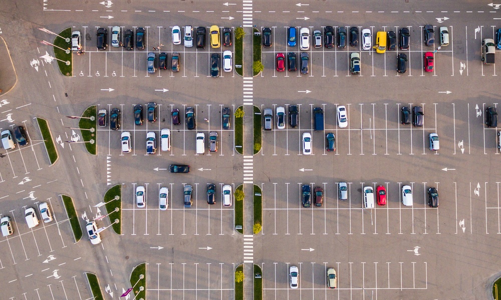 An aerial view of a commercial parking lot. There are many cars parked and they are all of varying colors and designs.