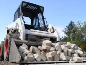 A front view of a skid steer loader pushing a pile of broken concrete blocks on a construction site.