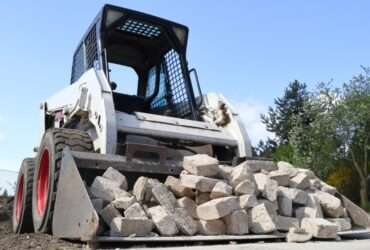 A front view of a skid steer loader pushing a pile of broken concrete blocks on a construction site.