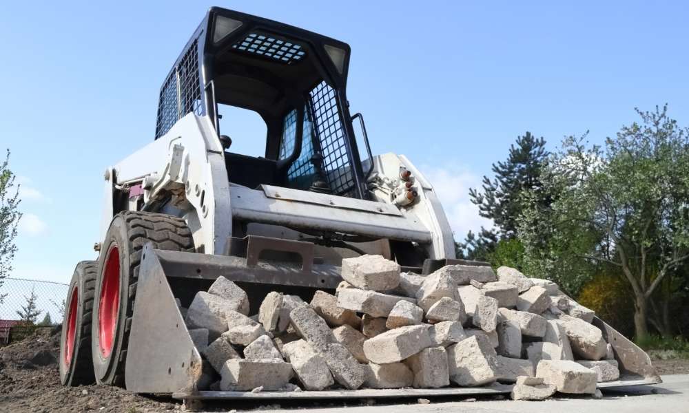A front view of a skid steer loader pushing a pile of broken concrete blocks on a construction site.