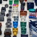 A collection of automotive electrical connectors lying on a white table. The connectors vary in size, shape, and color.