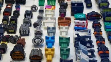 A collection of automotive electrical connectors lying on a white table. The connectors vary in size, shape, and color.
