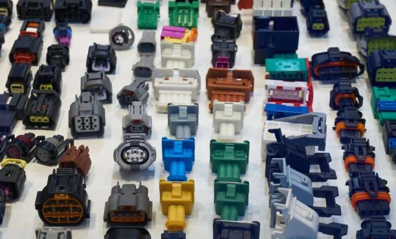 A collection of automotive electrical connectors lying on a white table. The connectors vary in size, shape, and color.