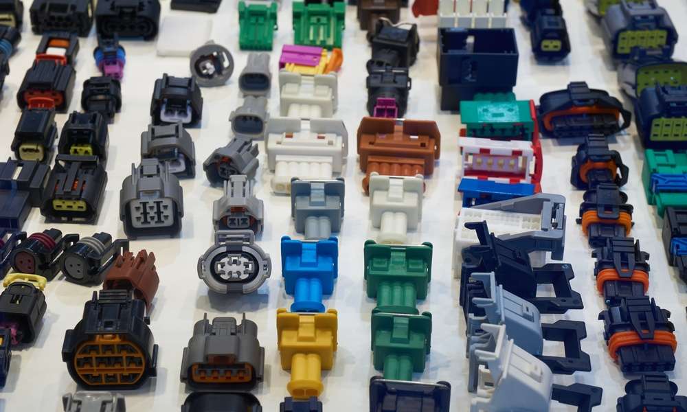 A collection of automotive electrical connectors lying on a white table. The connectors vary in size, shape, and color.