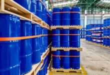 A warehouse full of blue chemical drums stacked on wooden pallets. The drums are brand new and shiny.