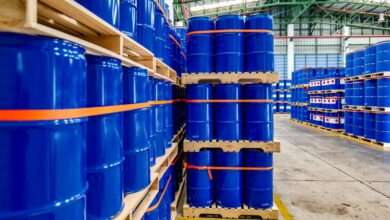 A warehouse full of blue chemical drums stacked on wooden pallets. The drums are brand new and shiny.