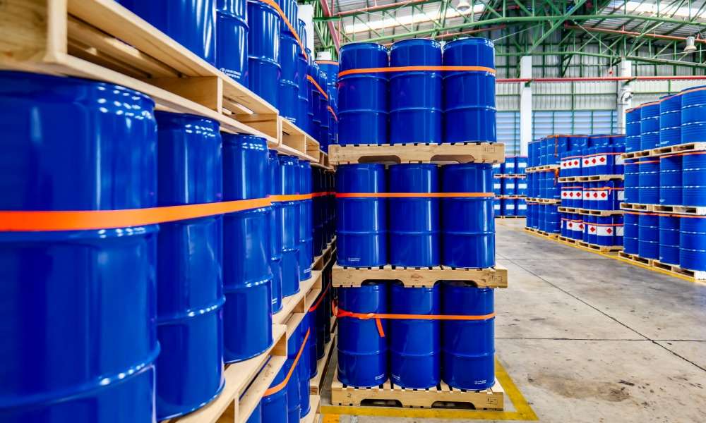 A warehouse full of blue chemical drums stacked on wooden pallets. The drums are brand new and shiny.