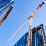 A large yellow crane standing on a construction site between two high-rise buildings in a city during the daytime.