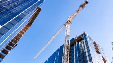 A large yellow crane standing on a construction site between two high-rise buildings in a city during the daytime.