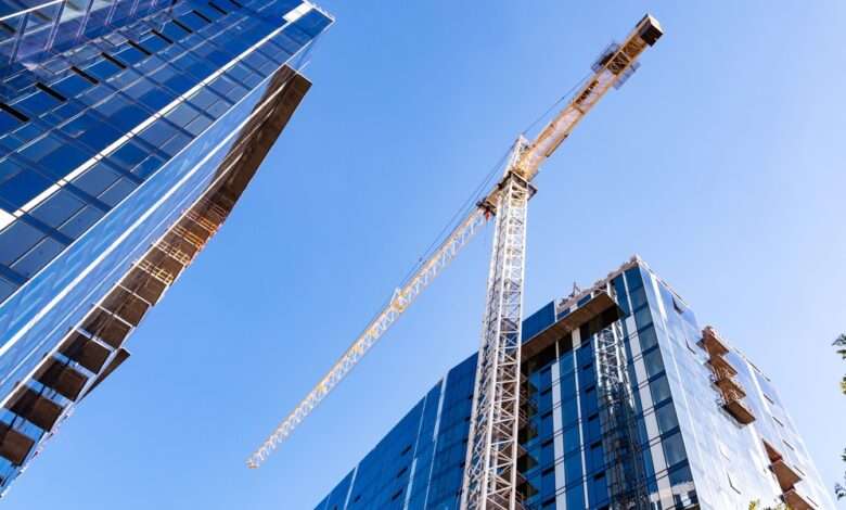 A large yellow crane standing on a construction site between two high-rise buildings in a city during the daytime.