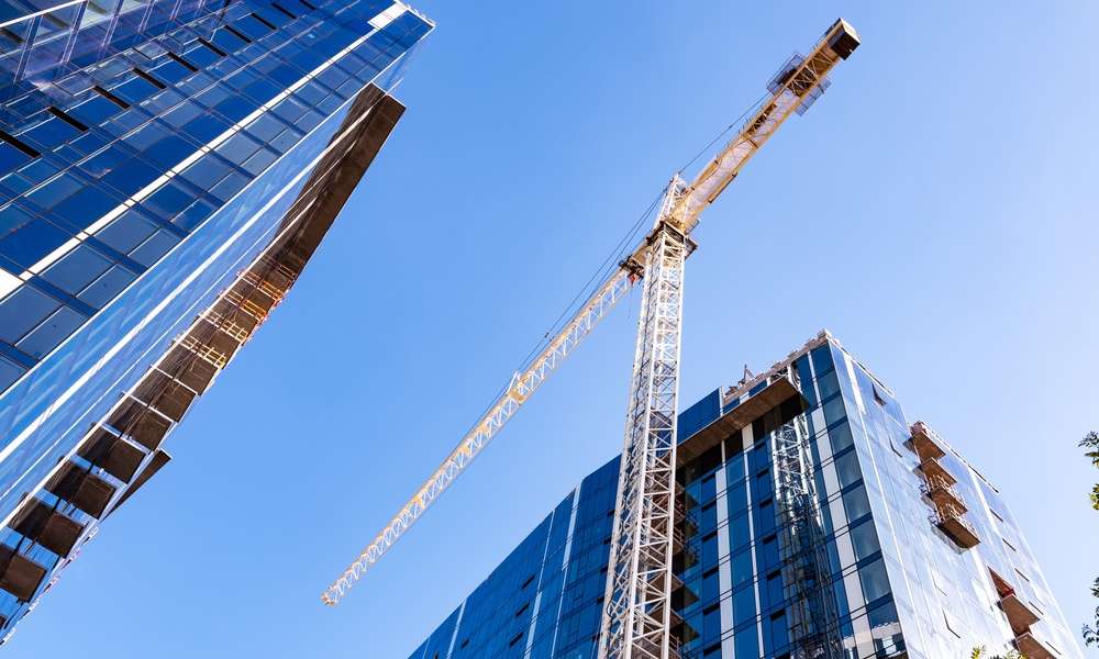 A large yellow crane standing on a construction site between two high-rise buildings in a city during the daytime.
