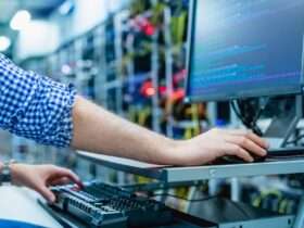 A man is sitting in front of a computer screen. In the background are tech components that are blurred.