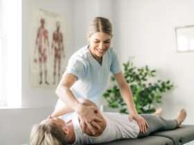 A woman is standing while physically manipulating another woman who is laying down on a table.