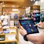 A manager holding a tablet with data and figures about store management. Behind the tablet is a store with apparel.