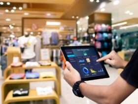 A manager holding a tablet with data and figures about store management. Behind the tablet is a store with apparel.