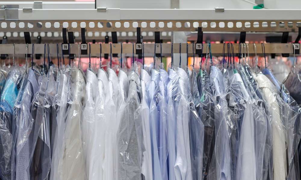 Several dress shirts are hanging on hangars and are placed on a rack. Each shirt has a plastic cover on them.