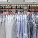 Several dress shirts are hanging on hangars and are placed on a rack. Each shirt has a plastic cover on them.