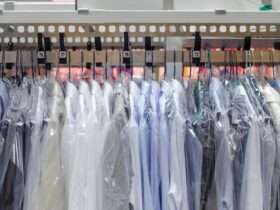 Several dress shirts are hanging on hangars and are placed on a rack. Each shirt has a plastic cover on them.