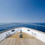 A close-up of the front of a large boat with a wooden cover and silver railing, with a view of the open ocean.