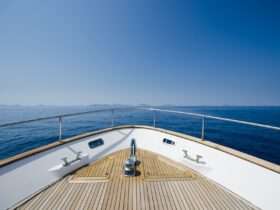 A close-up of the front of a large boat with a wooden cover and silver railing, with a view of the open ocean.
