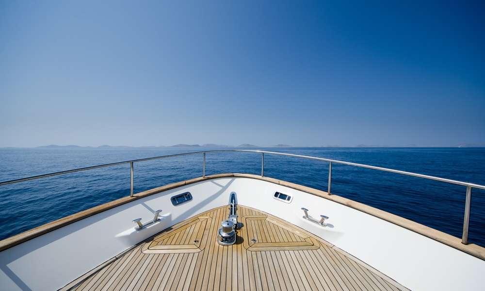 A close-up of the front of a large boat with a wooden cover and silver railing, with a view of the open ocean.