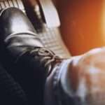 A close-up of someone pressing their foot against the brake pad of a car. The gas pedal is blurred.