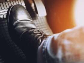 A close-up of someone pressing their foot against the brake pad of a car. The gas pedal is blurred.