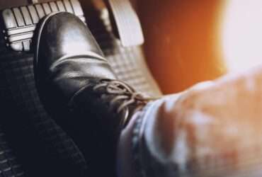 A close-up of someone pressing their foot against the brake pad of a car. The gas pedal is blurred.