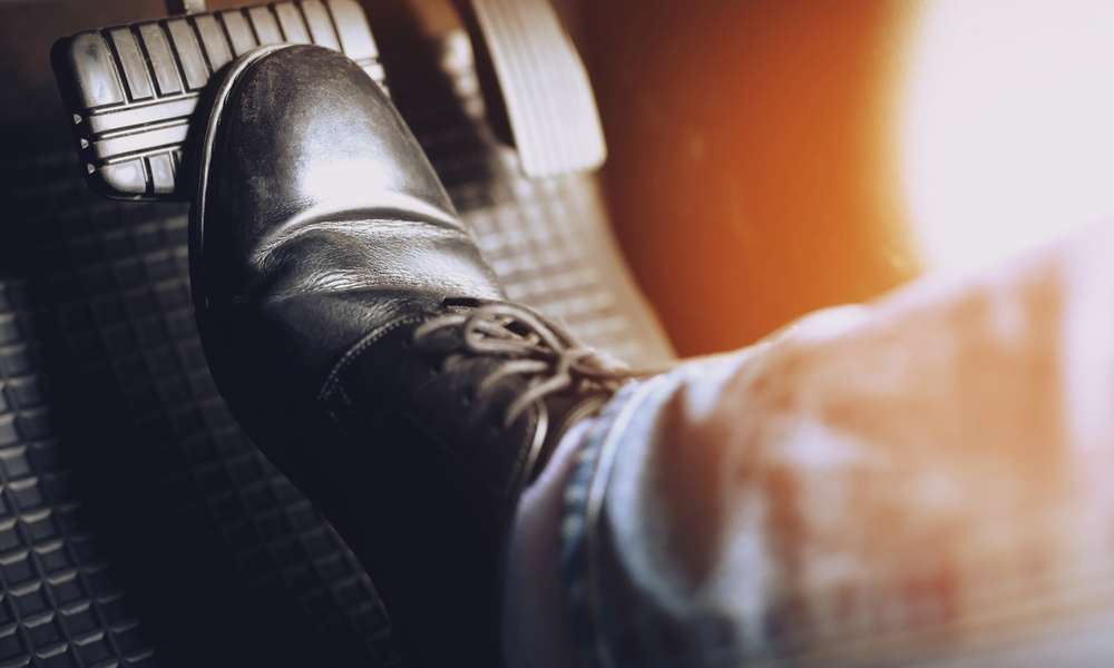 A close-up of someone pressing their foot against the brake pad of a car. The gas pedal is blurred.