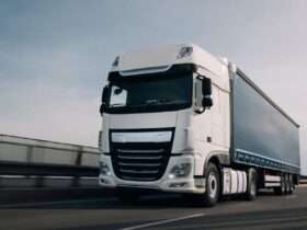 A semi truck with a cargo trailer driving along a highway with motion blur visible on the road and wheels.