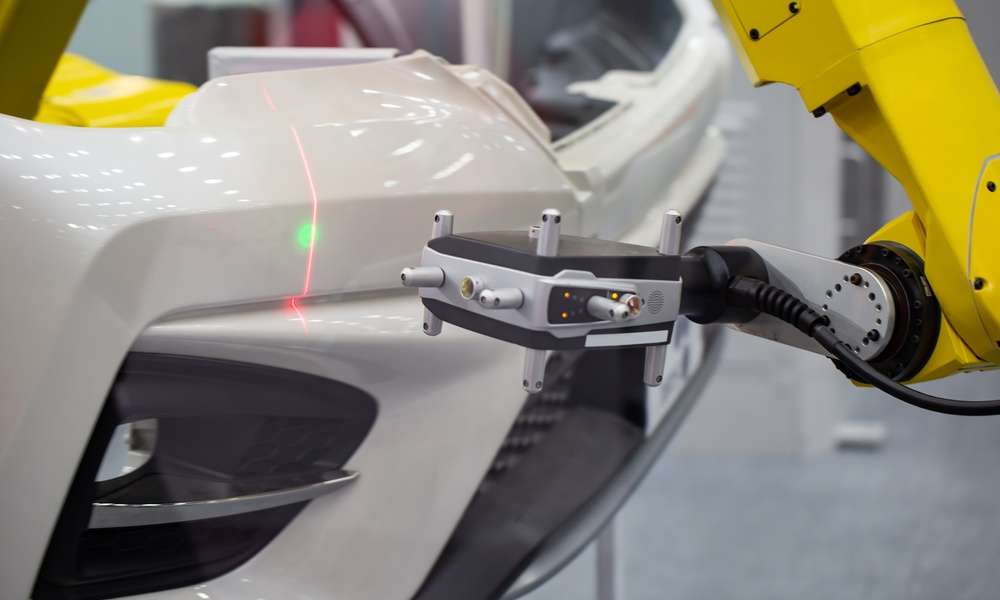A metrology laser measures a white bumper on a vehicle. There is a green dot and a red verticle line on the bumper.