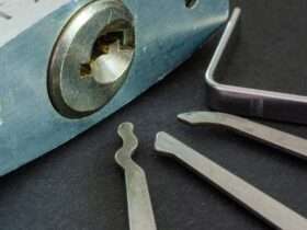 Close-up of a padlock sitting on a table, with its keyhole visible. Three silver metal picks sit next to it.