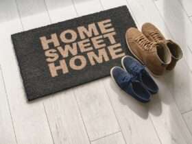 A pair of navy blue sneakers and a pair of brown boots sit on a mat on a tile floor that reads "Home Sweet Home."