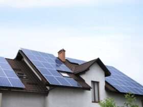 A residential home with multiple solar panel arrays installed across a sloped roof under a clear blue sky.