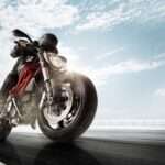 A person wearing a black jacket, black helmet, and black pants is driving a black motorcycle quickly.