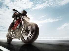 A person wearing a black jacket, black helmet, and black pants is driving a black motorcycle quickly.