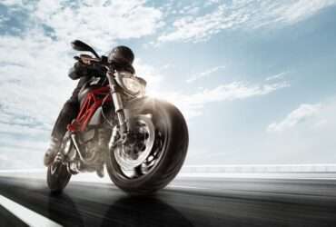A person wearing a black jacket, black helmet, and black pants is driving a black motorcycle quickly.