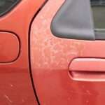 A red car door with faded paint that shows cracks and the underlayer. The damage is on other parts of the car.