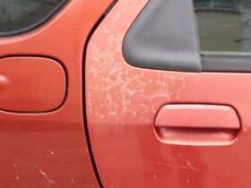 A red car door with faded paint that shows cracks and the underlayer. The damage is on other parts of the car.