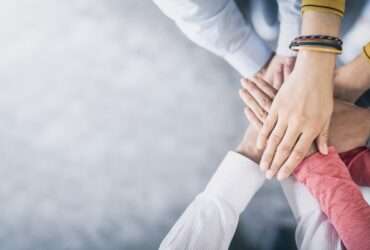 An aerial view shows several people placing their hands in the center of a circle, stacking them on top of each other.