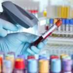 A close-up of a pair of hands with latex gloves using a barcode scanner to scan the barcode on a blood vial.