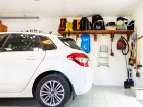 Interior garage with white hatchback, neatly arranged shelves, tools, vacuum, ladder, and storage items on wall.