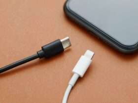 A close-up view shows a black USB-C charger and a white lightning charger sitting on a wooden surface by a smartphone.