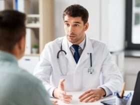 A doctor talking to a patient in their large office. The patient sits across a desk from the doctor.